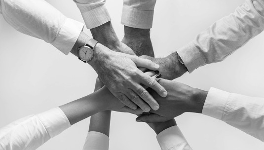 A group of employees with their hands in a circle showing teamwork.
